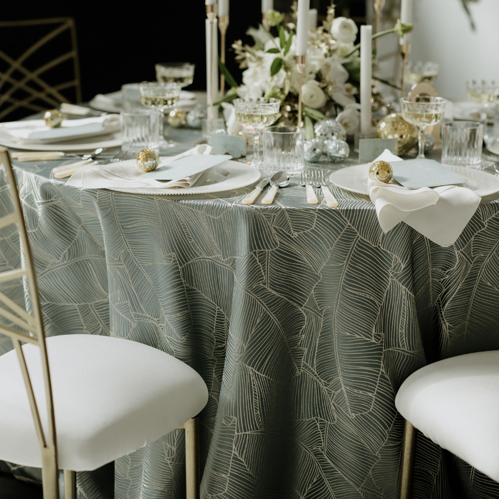 Nola White Napkins and Palmers Slate Tablecloth with metallic palm print in a blue-grey and gold-tone.