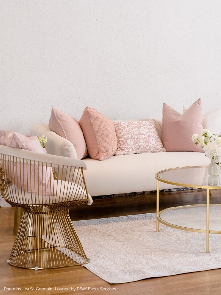 a couch with pink pillows and a gold chair