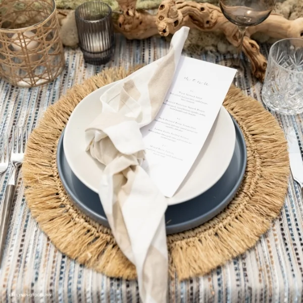 A table setting with a Dunes Striped Napkin and plates available for table linen rental.