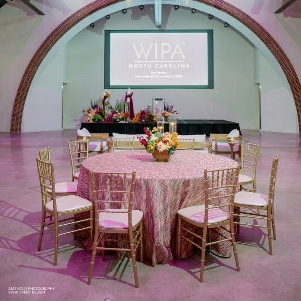 An elegant round Canyon Magenta table with chairs in front of a screen, perfect for events and available for table linen rental.