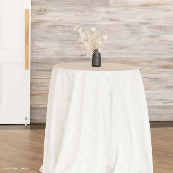 A Diem Grey table with a vase of flowers on it for an event linen rental.