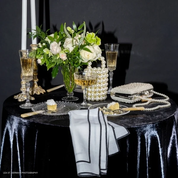 A sophisticated black and white table setting adorned with elegant flowers and a glass of champagne. Plus, you can find The Jules table linen rental or event linen rental to complete the look.