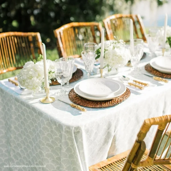 A white and gold table setting with rattan chairs, perfect for Lennon Powdered Blue event linen rental.