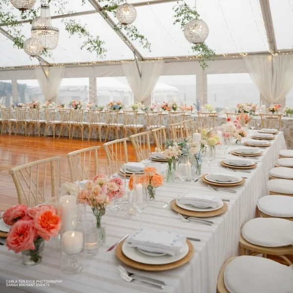 A table set up in a tent with white linens and Linea Sand flowers available for event Linea Sand rental.