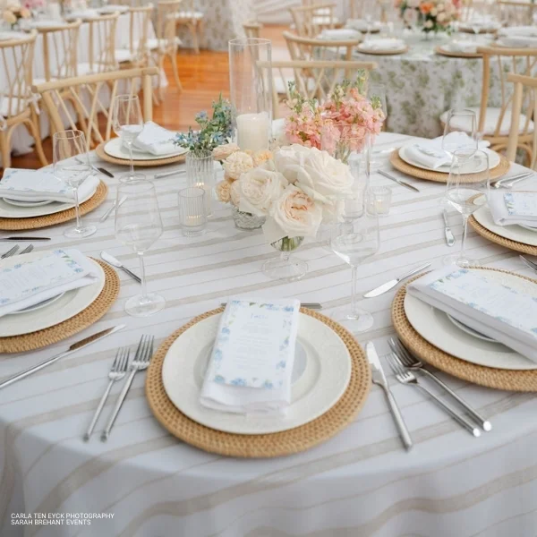 A table setting with white linens and pink flowers available for Linea Sand table linen rental.