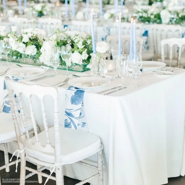 A blue and white wedding reception with white chairs featuring Livia Sapphire Napkin rental.