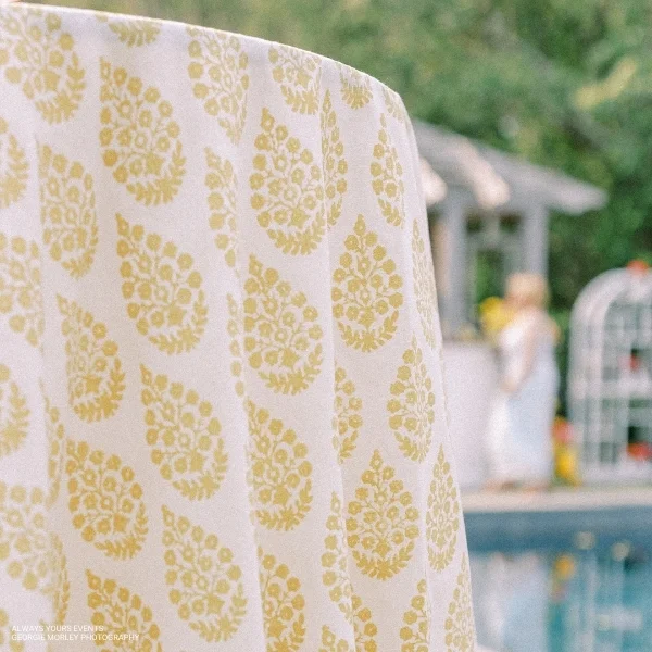 A Maisie Sunshine tablecloth with a yellow paisley pattern, perfect for event linen rental, placed near a pool.