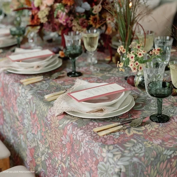 A table setting with a floral tablecloth and Country Lace Napkin place settings available for event linen rental.