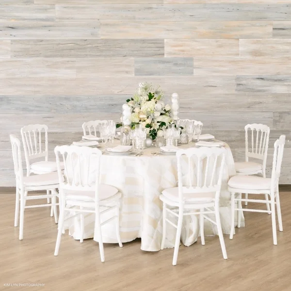A white table with white chairs and a wooden wall. The perfect setup for any event requiring Metropolitan Champagne rental.