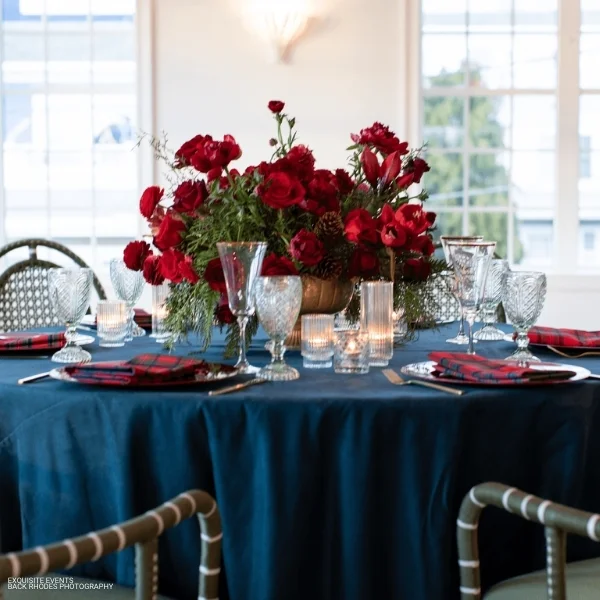An elegant table setting with red flowers on a Montana Suede Navy tablecloth, ideal for an event or party. Perfect for those in need of table linen rental.