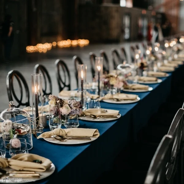A long table set with Montana Suede Navy table linens and candles, available for event linen rental.