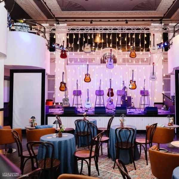 A room with tables and chairs, adorned with elegant Nola Mystic Blue table linen rentals, and a stage with guitars.