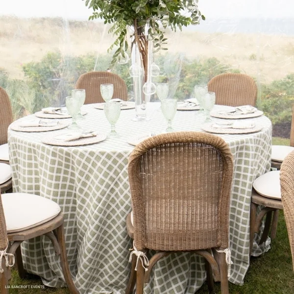 A table set up with a Patchwork Moss tablecloth rented from a linen rental service, adorned with a beautiful vase of flowers.
