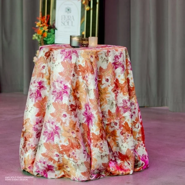 A table with a Penelope Pomegranate cloth and candles on it available for table linen rental.