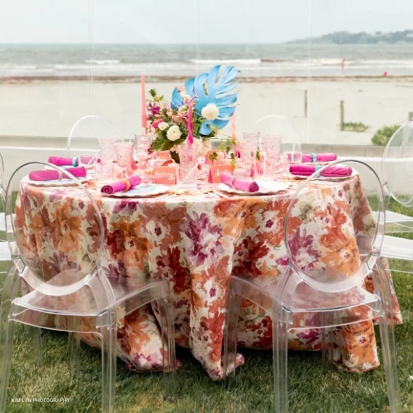 An event table adorned with clear chairs and a Penelope Pomegranate tablecloth rented from a table linen rental service.