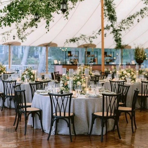 An arrangement of Riga Sand tables and chairs with table linen rental in a tent.