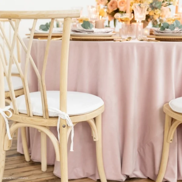 A table set up with a Velvet Blush tablecloth and chairs available for table linen rental.