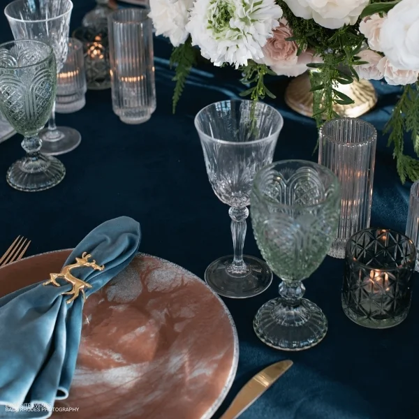 A table with Velvet Deep Sea event linen rental, including a plate and glasses.