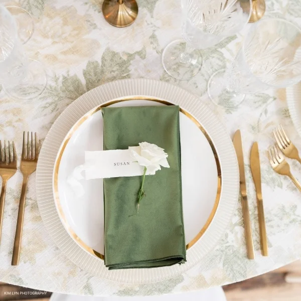 An elegant table setting featuring a Velvet Evergreen napkin and gold forks, available for table linen rental.