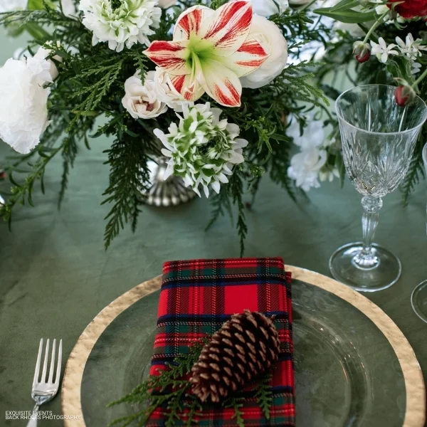 A festive holiday table setting adorned with Tartan Plaid Holly Berry Napkins and pine cones, perfect for a Christmas event or party. Whether you're looking for event linen rental or table linen rental, this stunning