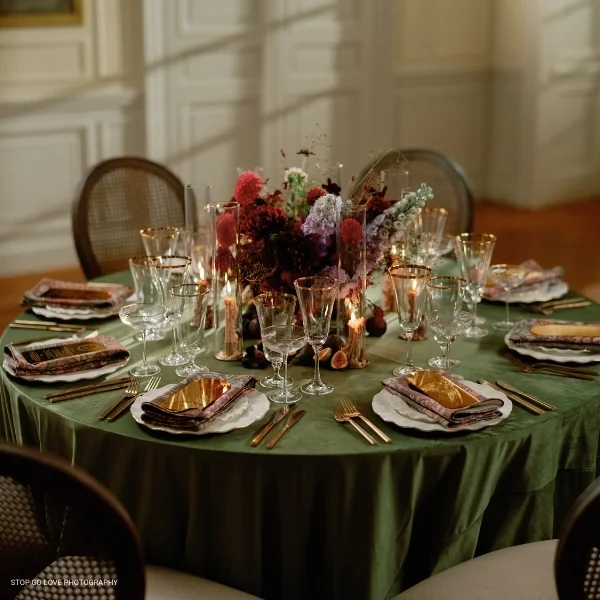 An elegant table setting with a Velvet Evergreen tablecloth and gold candlesticks, available for table linen rental.