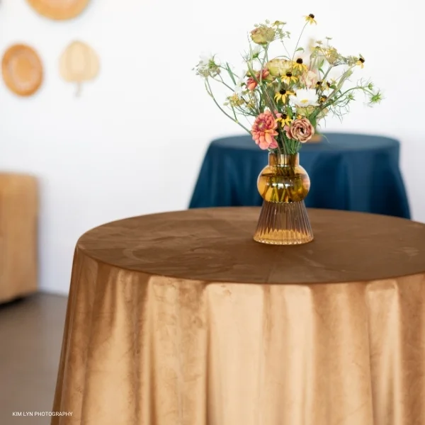 A table with a Velvet Hazel vase of flowers on it available for event linen rental.