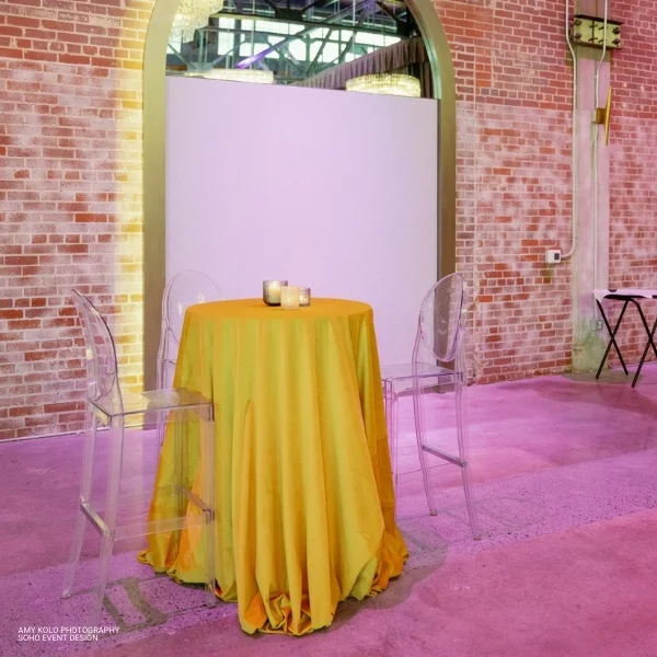 A room with a yellow Velvet Marigold table and chairs available for event linen rental in front of a brick wall.