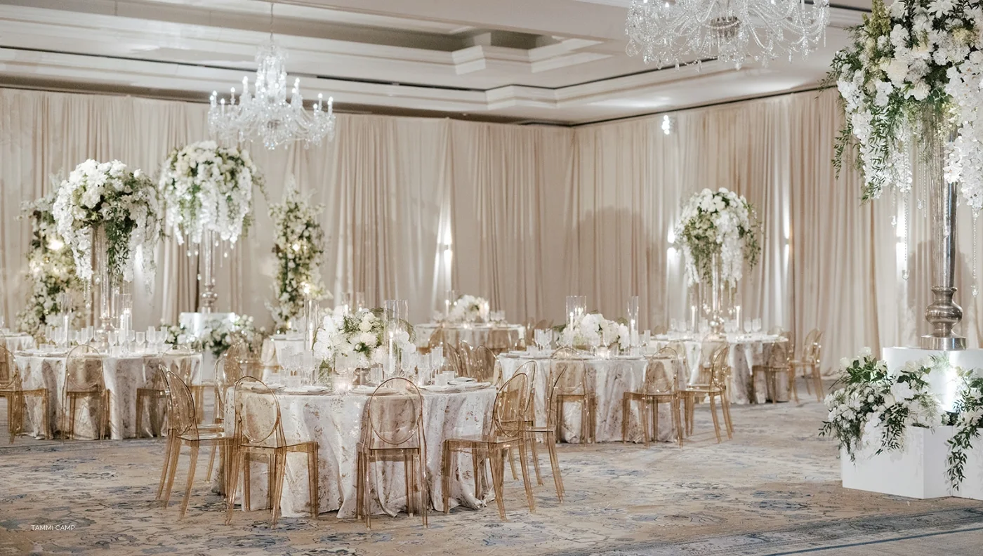 A white and gold ballroom decorated with flowers and chandeliers is the perfect setting for any event. Complete your elegant affair with our table linen rental service, providing luxurious linens that will