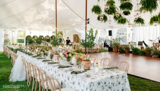 Elegant outdoor wedding reception setup under a white tent with floral decorations and arranged tables featuring the latest table linen trends.