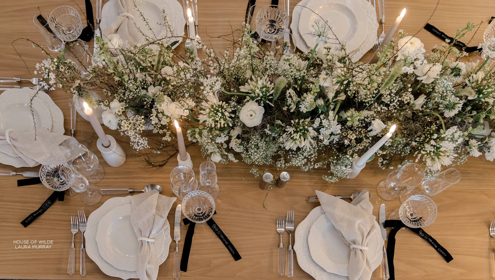 Elegant dining table setting with white florals, candles, and a rustic wooden table for a reverie social gathering.