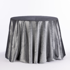 A Opulent Mist Velvet round table is adorned with a shiny silver tablecloth, set against a plain white background.