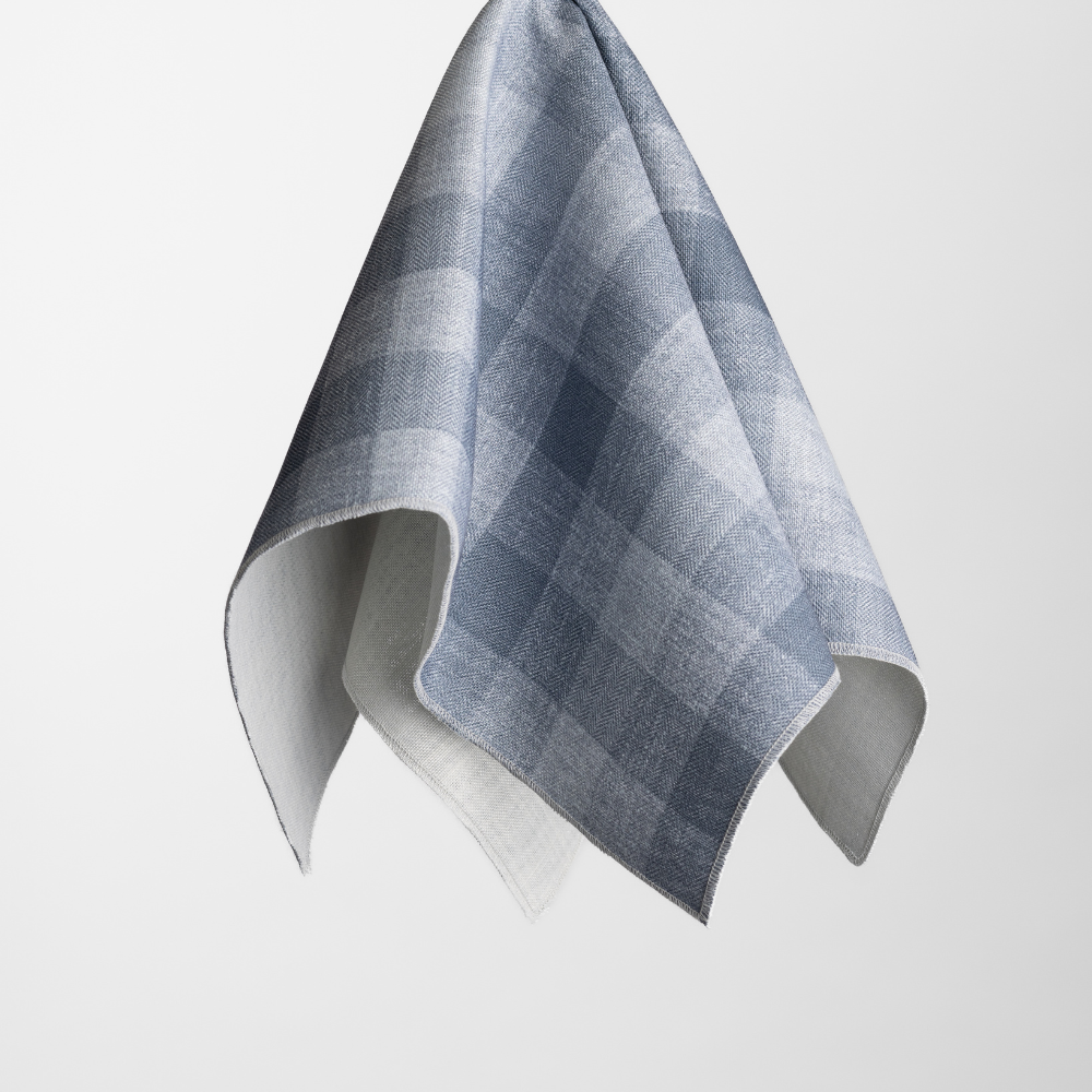The Checkered Plaid Harbor Napkin, featuring a blue and white plaid design, hangs against a plain white background.